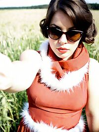 A 21 year old woman with short hair and a red dress lounges in a sunlit meadow