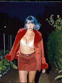 Tall woman in 1960s fashion poses curiously amidst moonlit vegetable garden shadows