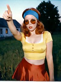 Woman in 1970s attire sporting ginger locks and D cup breasts in an old farmhouse