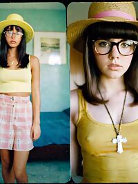 A young woman in a yellow tank top stands surprised in a retro motel room at noon